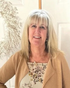 Smiling blonde woman in a beige cardigan with a leopard-print top, indoors.