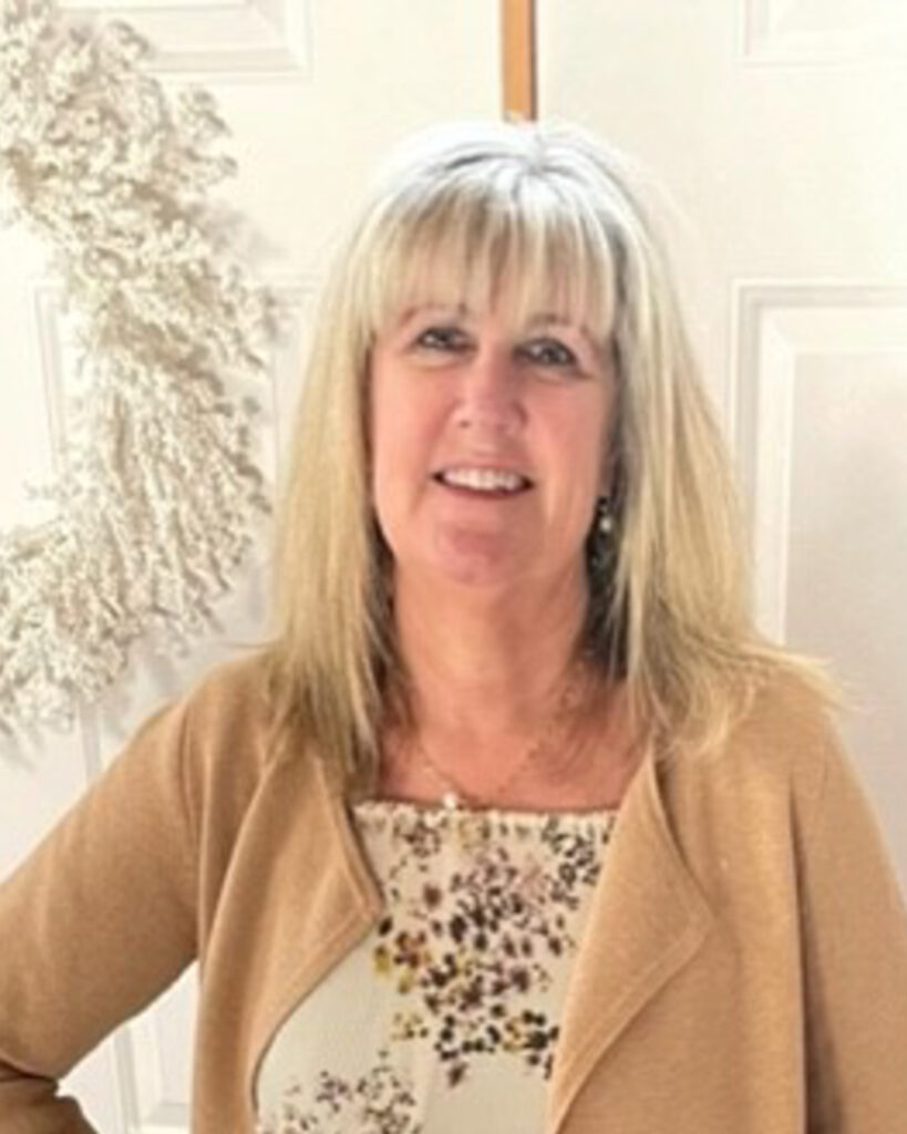 Smiling blonde woman in a beige cardigan with a leopard-print top, indoors.